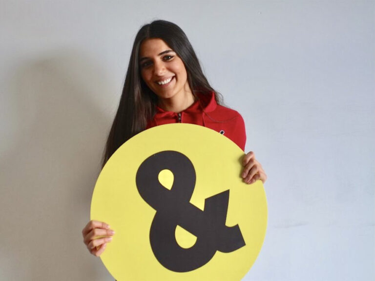 Geschäftsführerin Muna Nasser hält rundes, gelbes Schülerpatenlogo in den Händen